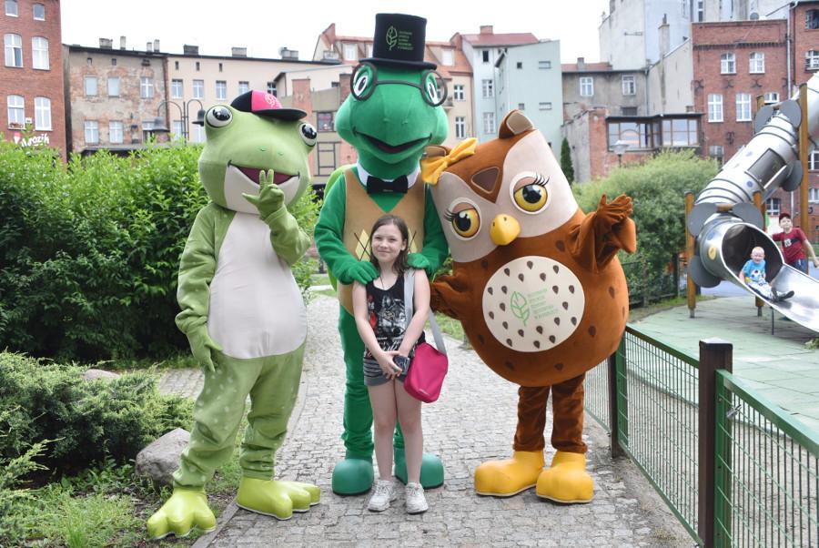 Żywe maskotki: żaba, żółw i sowa pozują do zdjęcia z dziewczynką z różową torbą