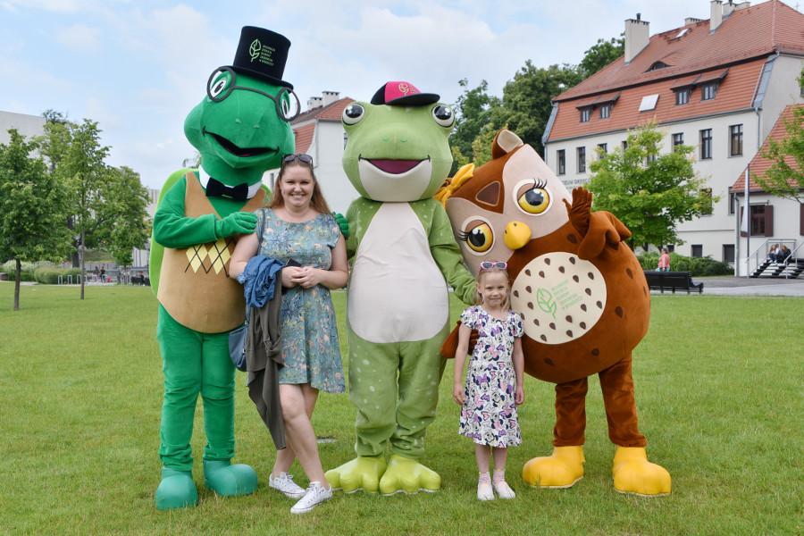 Żywe maskotki: żółw, żaba i sowa pozują do zdjęcia z mamą z córką w kwiecistych sukienkach